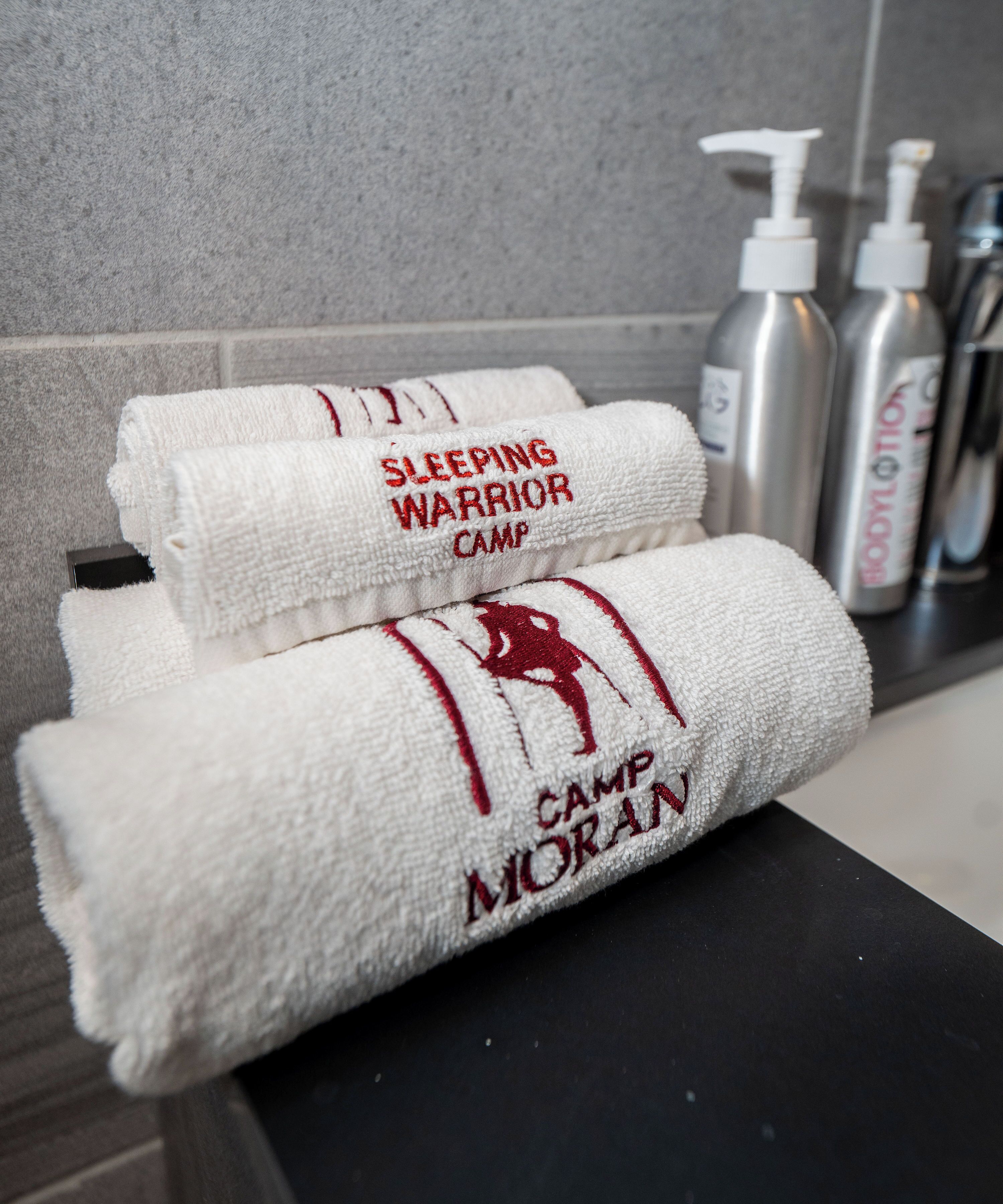 Neatly folded towels with embroidered text, a black countertop, and toiletries in the background.