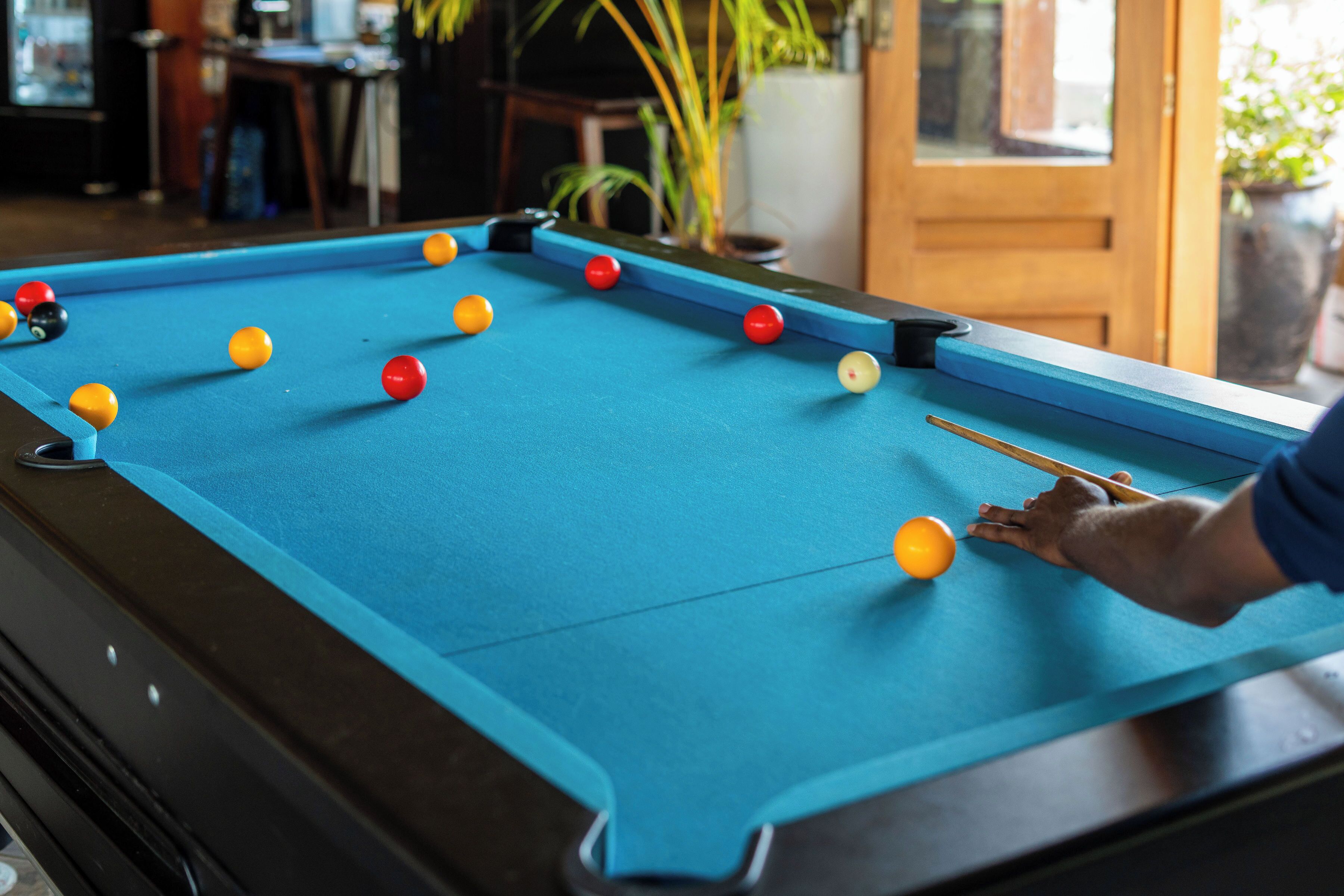 Une table de billard avec des billes, une personne qui joue, et une porte en arrière-plan.