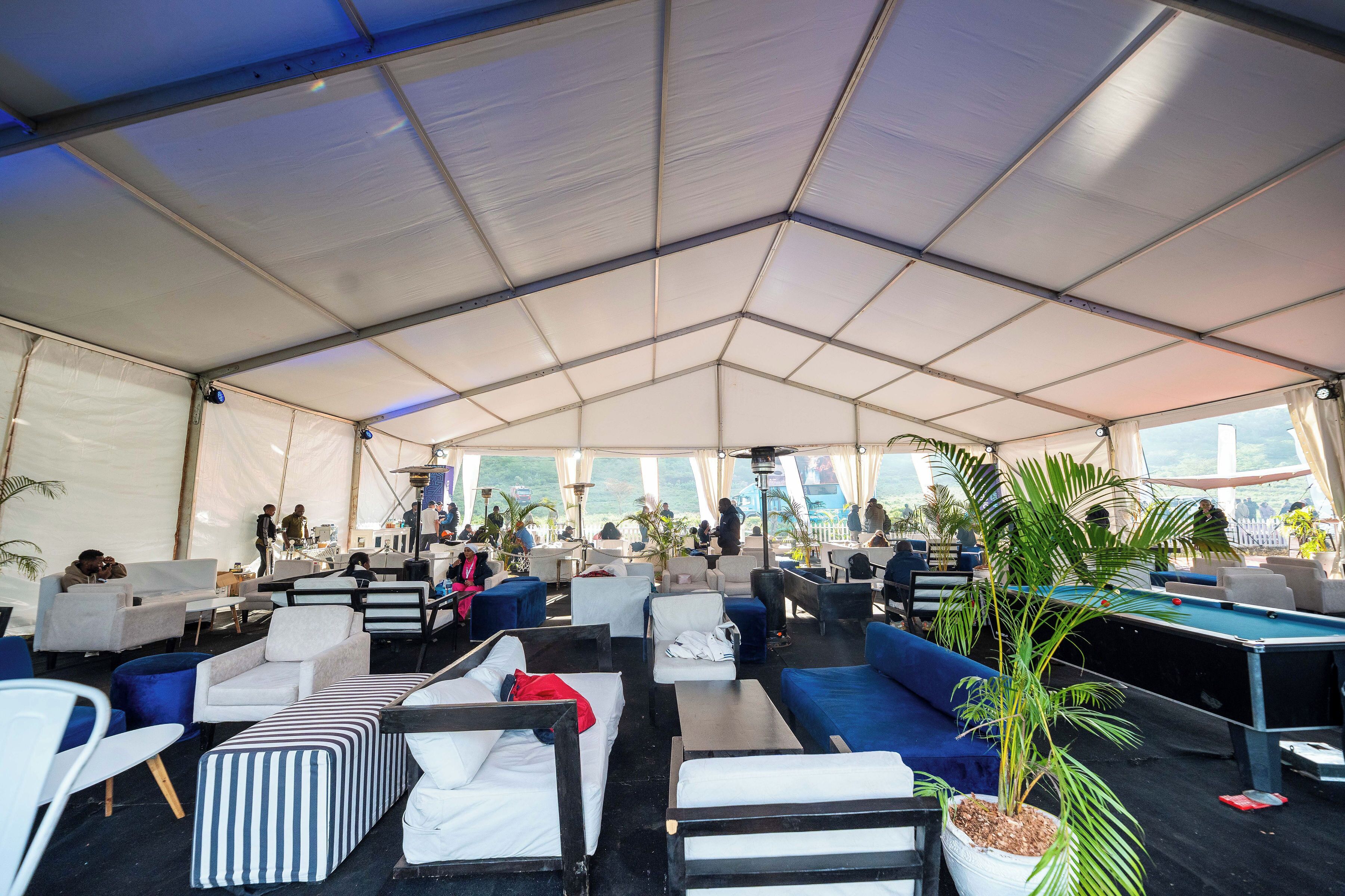 A tented lounge area with sofas, chairs, a pool table, and potted plants.