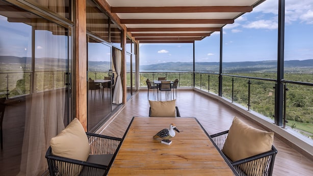 A spacious balcony with a wooden table, chairs, and a bird sculpture. - Sleeping Warrior Camp Elementaita (Gilgil)