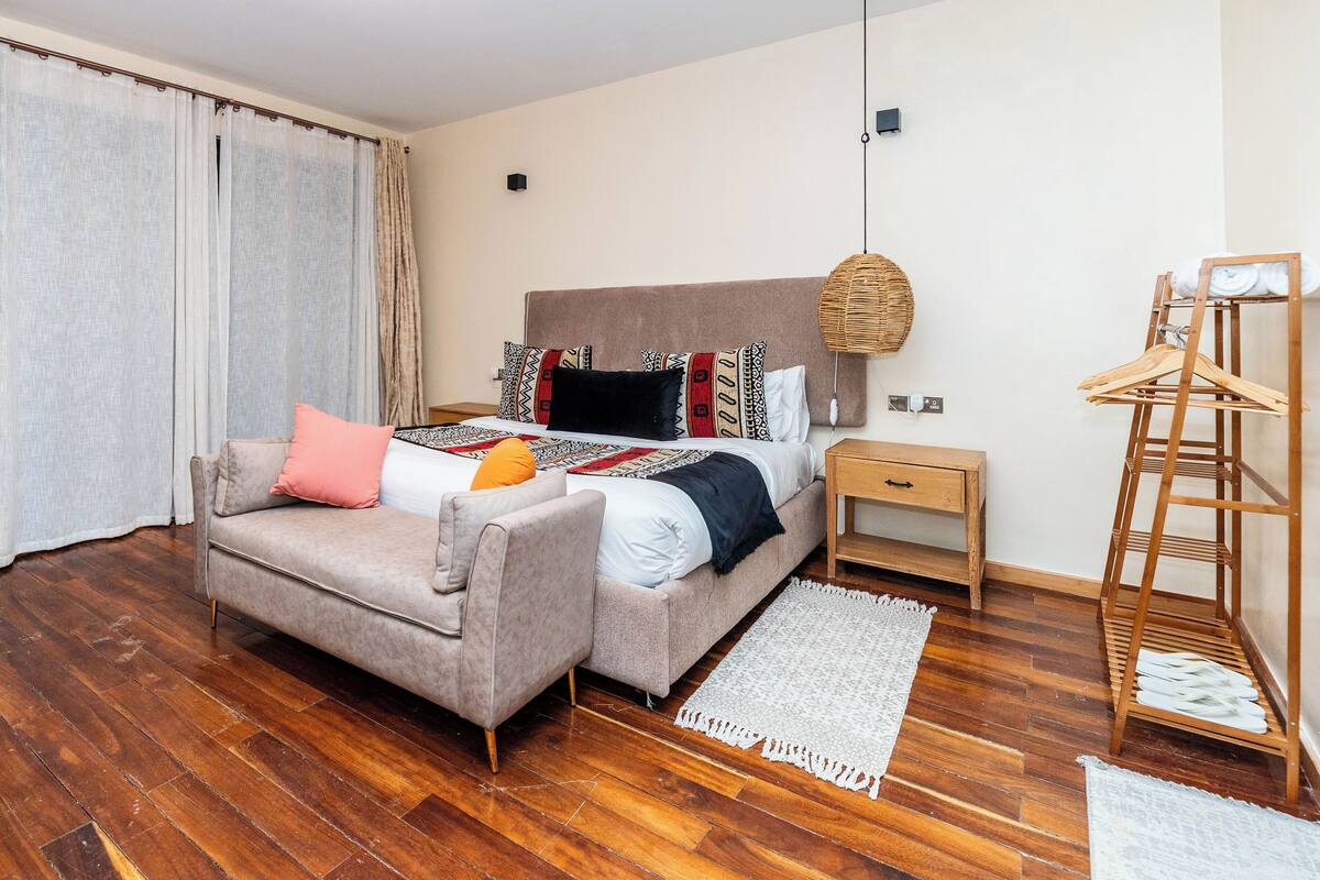 Ein Schlafzimmer mit einem Bett, einer Couch, einem Nachttisch aus Holz, einer Pendelleuchte und einem Kleiderständer aus Holz.