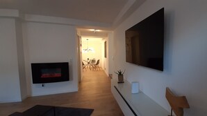 Ein modernes Wohnzimmer mit einem an der Wand befestigten Flachbildfernseher, einem Kamin und einem Essbereich im Hintergrund.