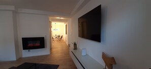 Una sala de estar moderna con un televisor de pantalla plana en la pared, una chimenea y un comedor al fondo.