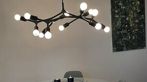 Ein Essbereich mit einem runden Glastisch, zwei grauen Stühlen, einer schwarzen Pendelleuchte und einem schwarzen abstrakten Gemälde an der Wand.
