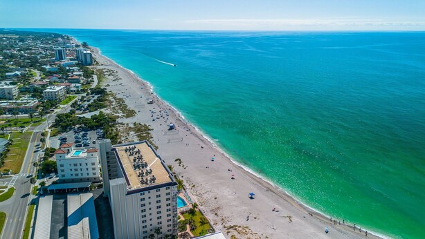 Vista aérea de una zona costera con playa, edificios y mar azul cristalino.