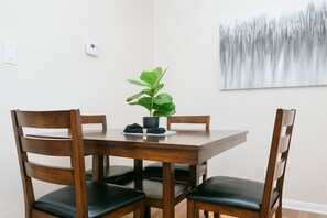 Un comedor con una mesa de madera y cuatro sillas, una planta en maceta y un cuadro en la pared.