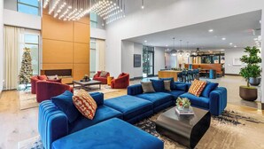 Un hall d’entrée spacieux, avec un canapé d’angle bleu, des fauteuils rouges et une grande plante en pot.