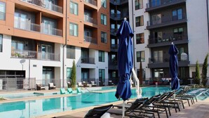 Et moderne hotel med swimmingpool, liggestole og blå parasoller.