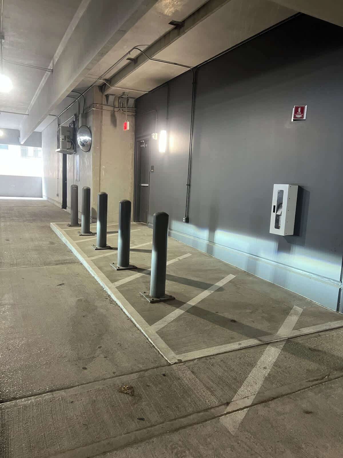Un estacionamiento con pisos de concreto, pilares y un detector de incendios instalado en la pared.