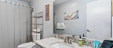A modern bathroom with a white toilet, a granite countertop sink, a large mirror, and a shower curtain.