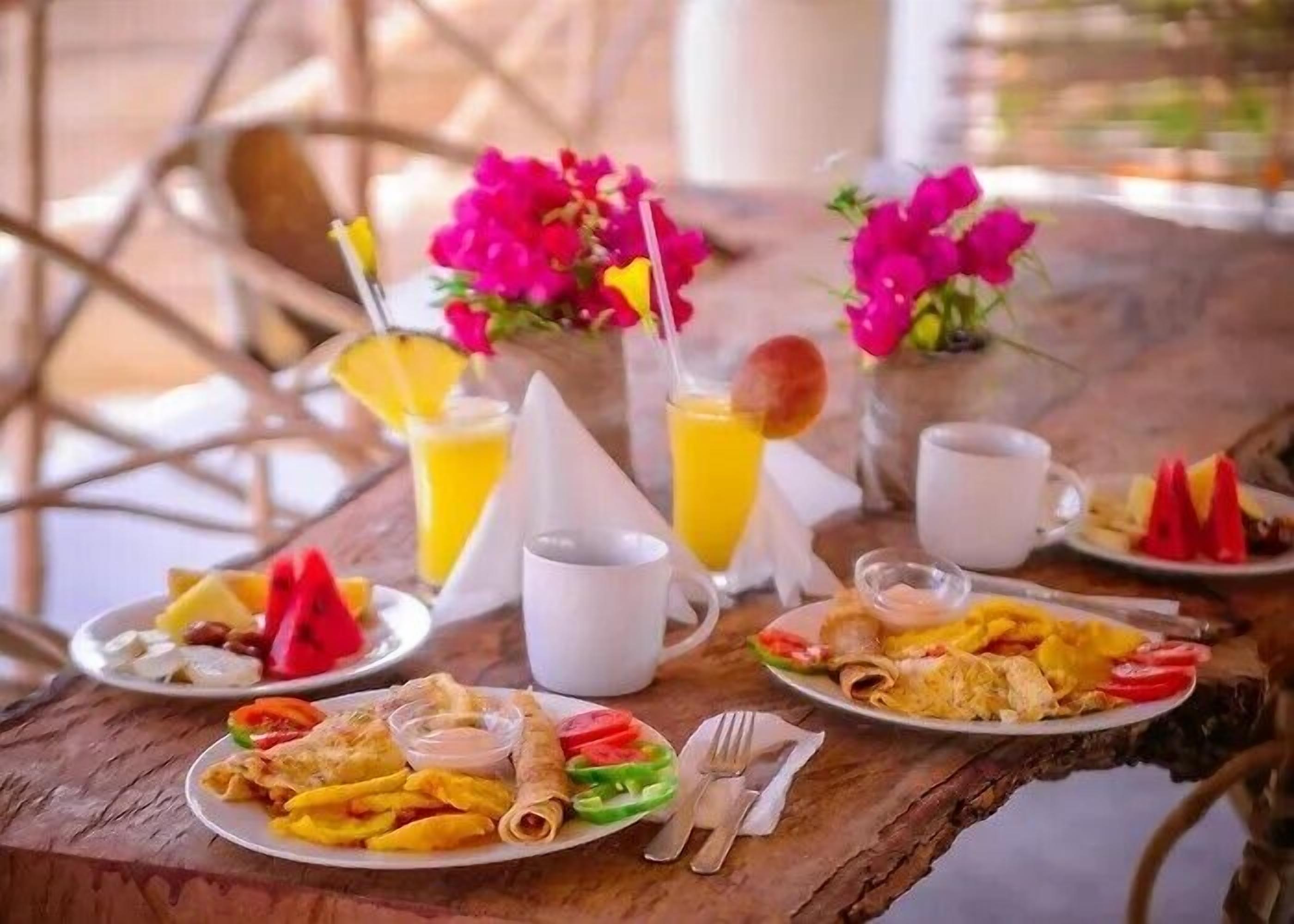 Una mesa de desayuno con platos de comida, bebidas y un jarrón de flores.