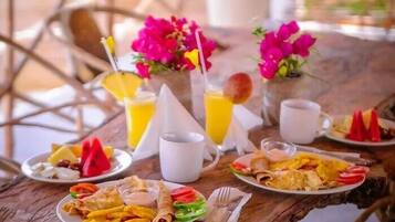 Una mesa de desayuno con platos de comida, bebidas y un jarrón de flores.