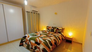 Quarto com cama, mesa de cabeceira, abajur, guarda-roupa e ar condicionado.