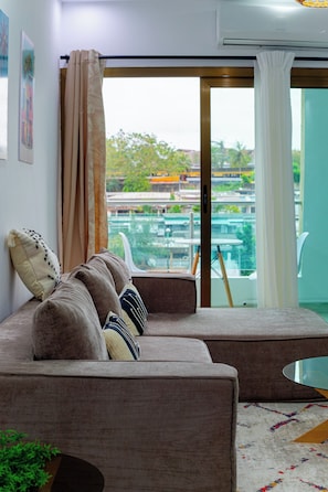 Een moderne woonkamer met een bank, een glazen salontafel en uitzicht op een zwembad en groen.