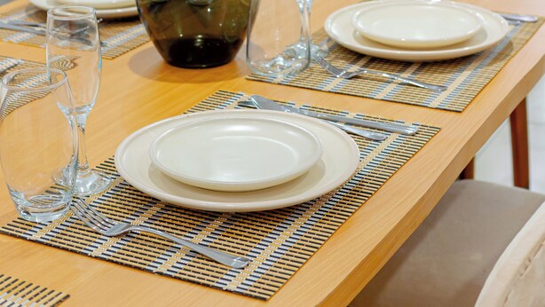 Uma mesa de jantar posta com pratos, copos e um vaso.
