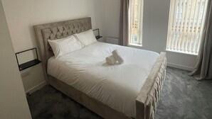 A neatly made bed with a headboard, a bedside table, a hanging light fixture, and a window with blinds. - Maison 109 Suite (Glasgow)