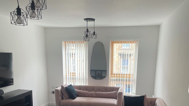 A living room with a large sofa, an ottoman, a small table, and a TV. - Maison 109 Suite (Glasgow)