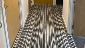 A hallway with a striped carpet, a yellow door, and a modern pendant light. - Maison 109 Suite (Glasgow)