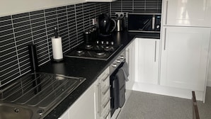 A modern kitchen with white cabinets, black countertops, a stainless steel sink, a stove, and an oven. - Maison 109 Suite (Glasgow)