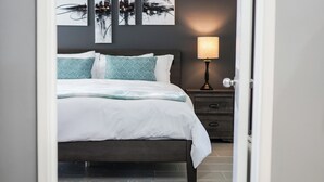 A neatly made bed with white bedding and patterned pillows, a bedside table with a lamp, and abstract wall art above the bed. - Cozy 2-bedroom condo in peaceful studio city with AC (Burbank)