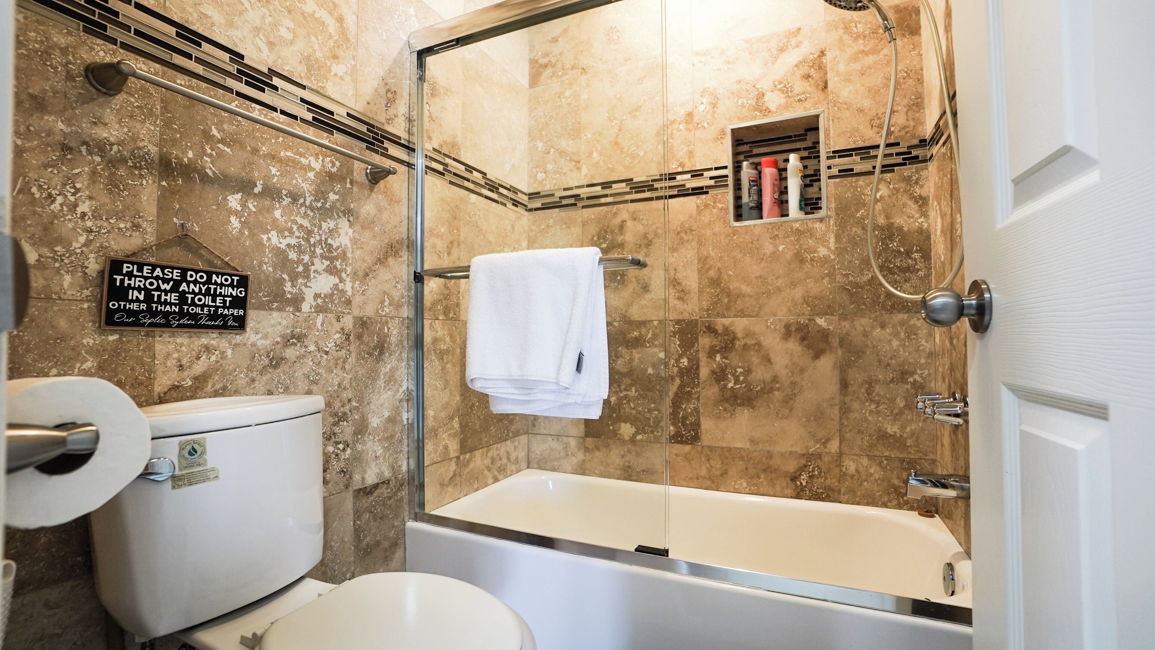 A bathroom with a toilet, a shower, and a bathtub. There is a sign on the wall and a towel rack.