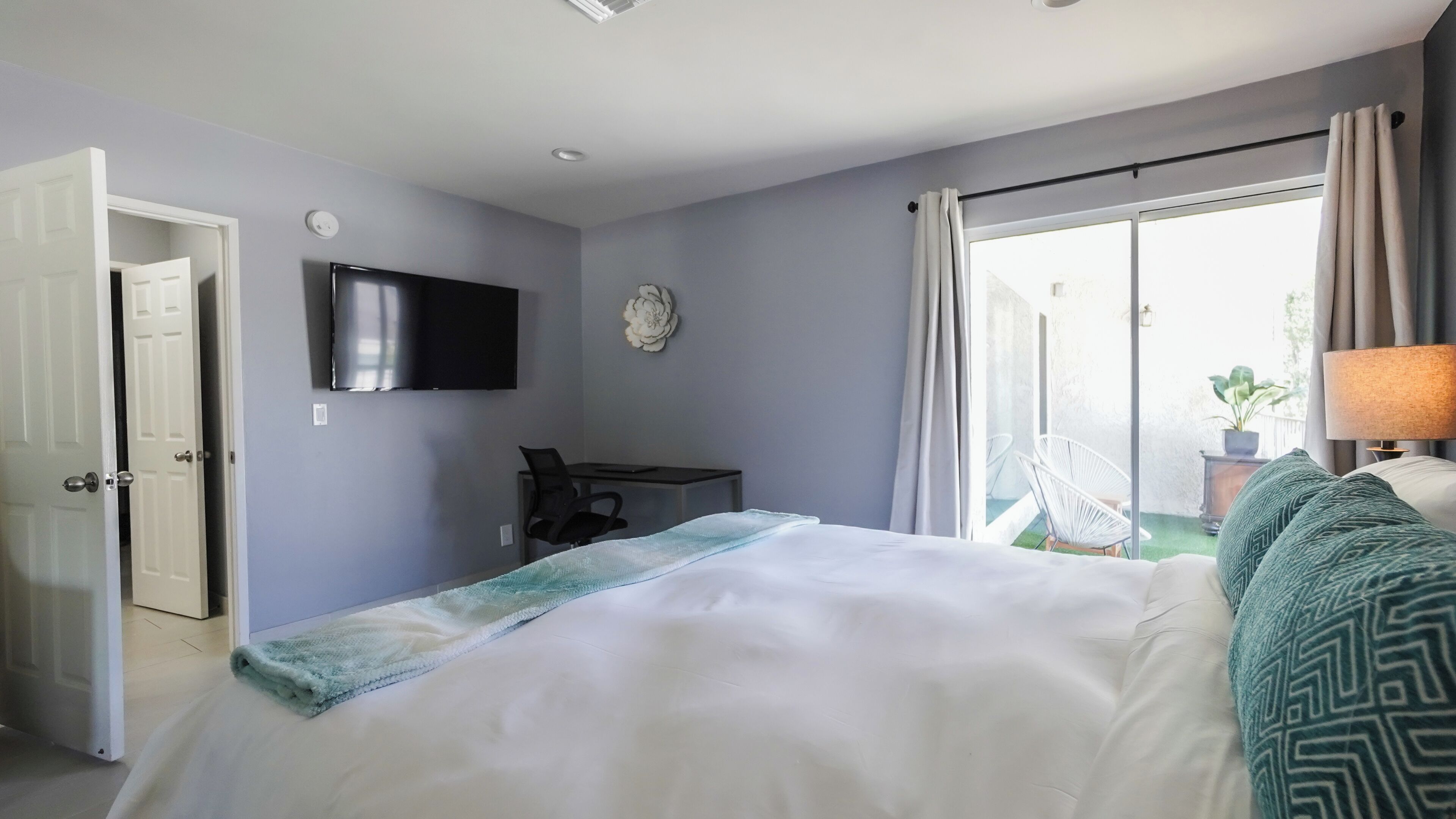 Habitación de hotel con cama, escritorio, silla, televisor y vistas al exterior.