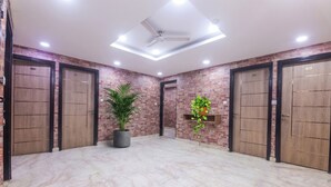 A spacious lobby with four wooden doors, a ceiling fan, recessed lighting, and potted plants. - Hotel om international  (New Delhi)