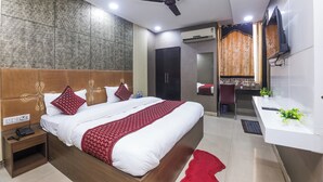 A modern hotel room with a large bed, a ceiling fan, a TV, a desk, and a bathroom visible through an open door. - Hotel om international  (New Delhi)
