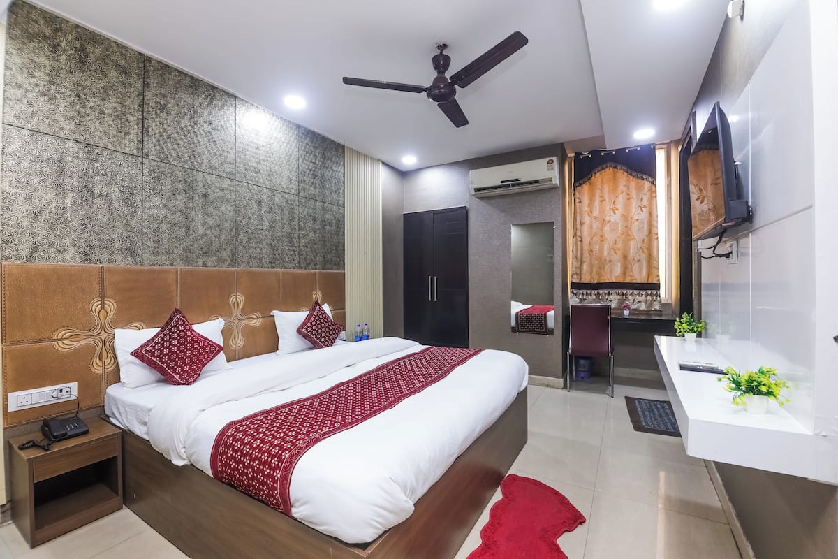 A modern hotel room with a large bed, a ceiling fan, a TV, a desk, and a bathroom visible through an open door.