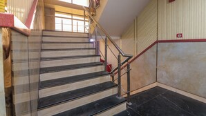 A staircase with metal railings, a red handrail, and a beige wall with a red stripe. - Hotel om international  (New Delhi)