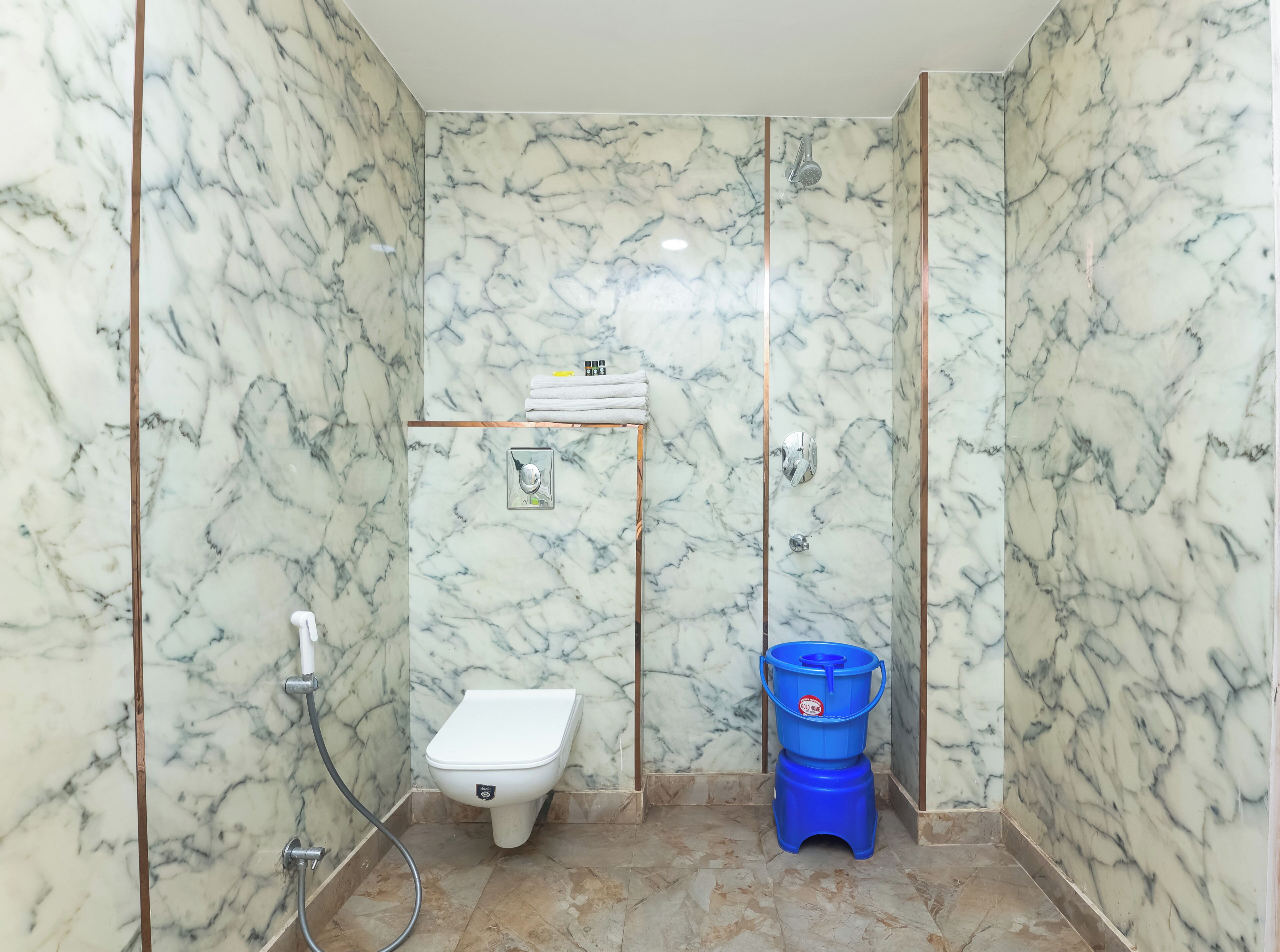 A bathroom with marble walls, a toilet, a shower, and a blue water container.