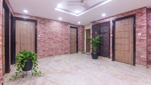 A lobby with brick walls, wooden doors numbered 201 and 204, a ceiling fan, and potted plants. - Hotel om international  (New Delhi)