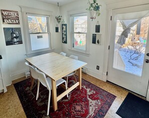 A dining area with a wooden table and chairs, a red patterned rug, and a view of the outside through a door. - Charming 3 Bedroom Victorian near Chain of Lakes & Greenway! (Minneapolis)