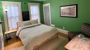 Une chambre à coucher avec un lit, un bureau, une chaise, une lampe et un tableau encadré au mur.