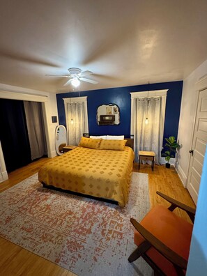 A bedroom with a bed, a ceiling fan, a bedside table, a chair, and a potted plant. - Charming 3 Bedroom Victorian near Chain of Lakes & Greenway! (Minneapolis)