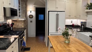 Une cuisine moderne avec des meubles blancs, un mur d’accent en pierre, une table en bois et un réfrigérateur en acier inoxydable.