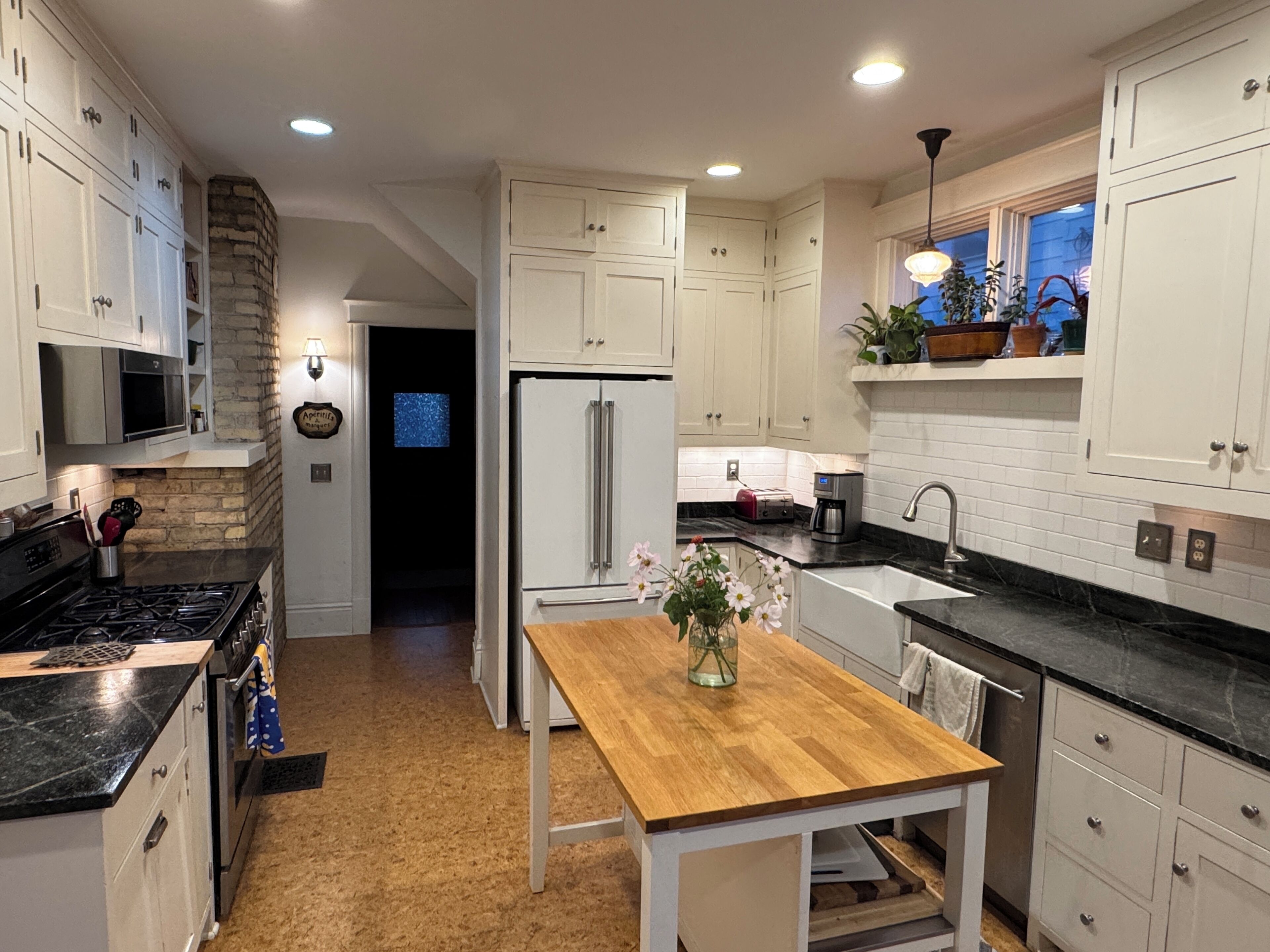 A kitchen with white cabinets, a wooden table, a refrigerator, a stove, and a sink.