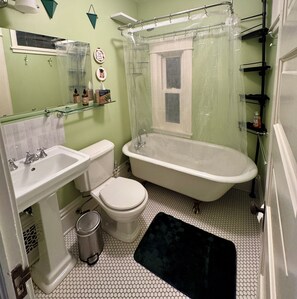 A bathroom with a toilet, sink, bathtub, and a glass shelf with toiletries. - Charming 3 Bedroom Victorian near Chain of Lakes & Greenway! (Minneapolis)