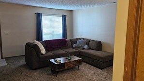 A living room with a sectional sofa, a coffee table, and a window with curtains. - 3-bedroom house in lancaster. (Lancaster)