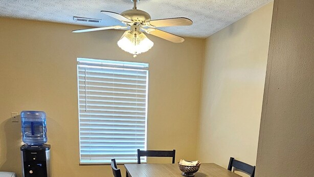 A dining area with a table and chairs, a ceiling fan, a water dispenser, and a window with blinds. - 3-bedroom house in lancaster. (Lancaster)