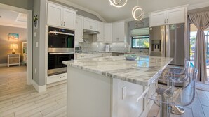 A modern kitchen with white cabinets, stainless steel appliances, and a marble island. - Villa Sunny Dream - New Villa - perfect for families and boaters (Cape Coral)