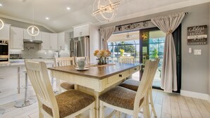 A modern kitchen with white cabinets, stainless steel appliances, and a wooden dining table with four chairs. - Villa Sunny Dream - New Villa - perfect for families and boaters (Cape Coral)