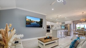 A modern living room with a sofa, a coffee table, and a TV mounted on the wall displaying a scenic view. - Villa Sunny Dream - New Villa - perfect for families and boaters (Cape Coral)