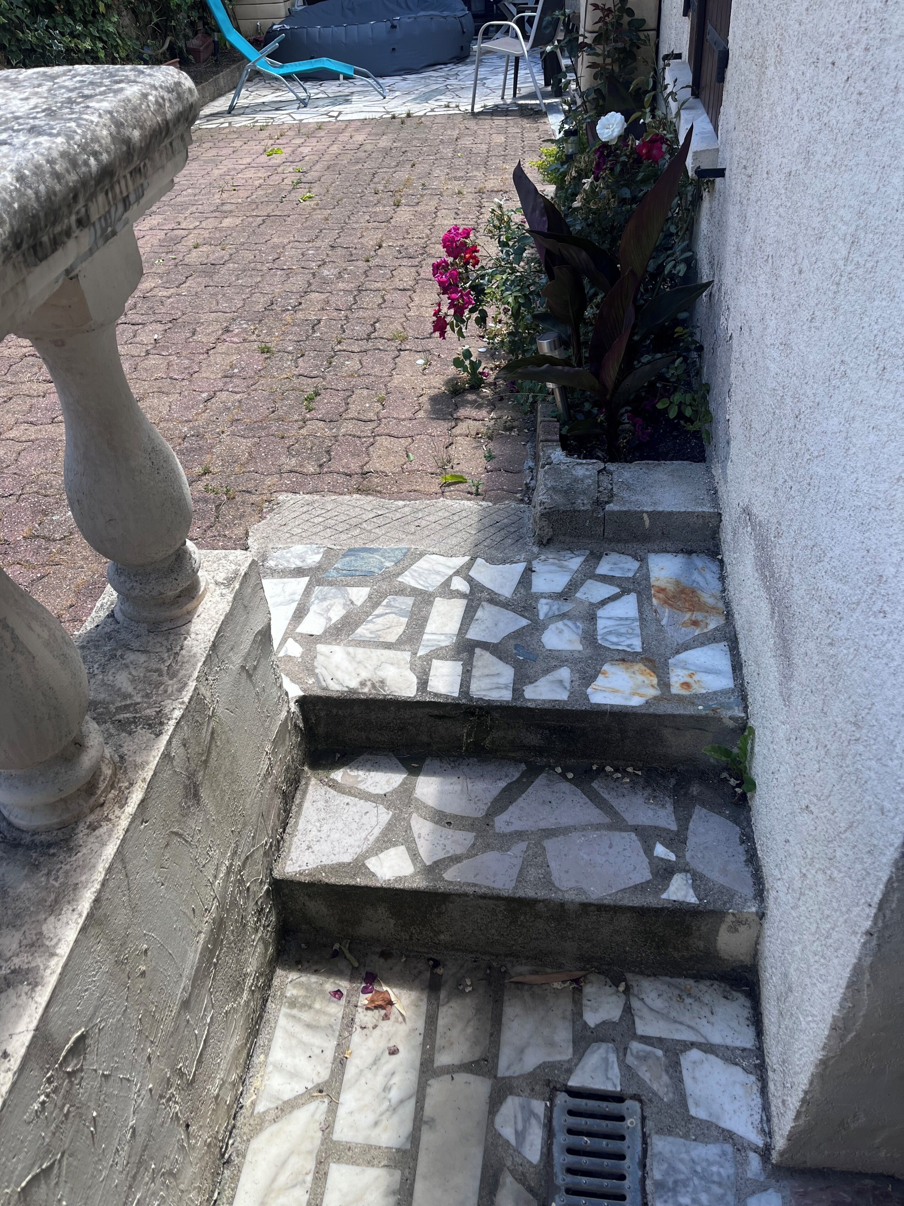 Eine Steintreppe führt zu einem Hauseingang, ein Garten mit Blumen und ein blauer Stuhl.