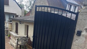 A gated entrance with a stone wall, a paved pathway, and a bench.