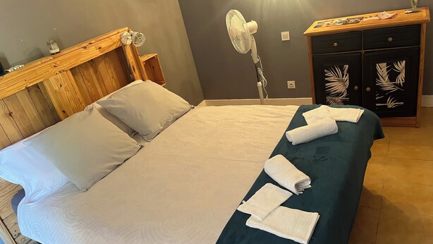 A neatly made bed with pillows, a bedside fan, and a wooden headboard.
