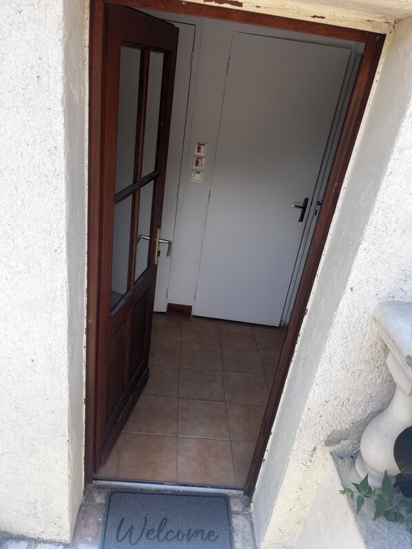 Une porte d’entrée en bois, un mur blanc, un sol carrelé et un paillasson.