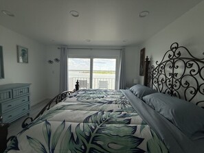 Ein Schlafzimmer mit einem Bett, einem Schminktisch und Blick auf das Wasser durch das Fenster.