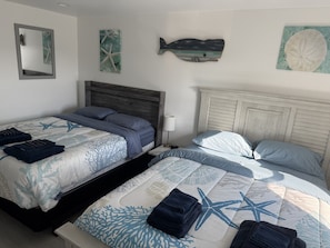 Ein Doppelbett mit einem Seestern- und Korallenmuster, ein Nachttisch und eine an der Wand befestigte Fischdekoration.