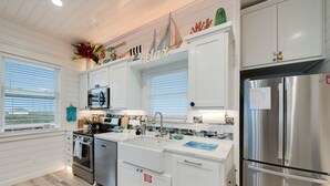 A modern kitchen with white cabinetry, stainless steel appliances, and a large window with blinds.